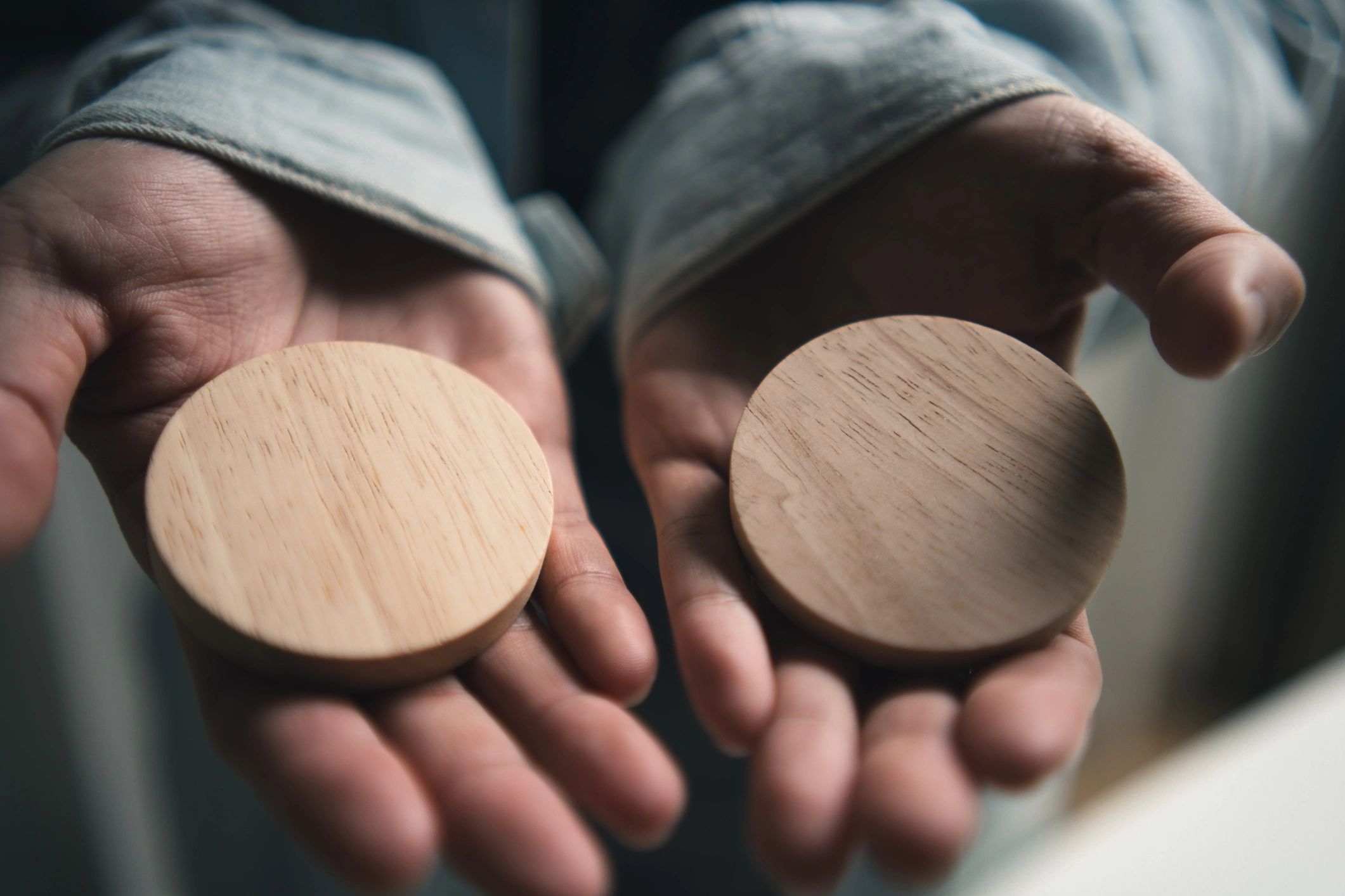 Hands holding blank circular wooden blocks for customization